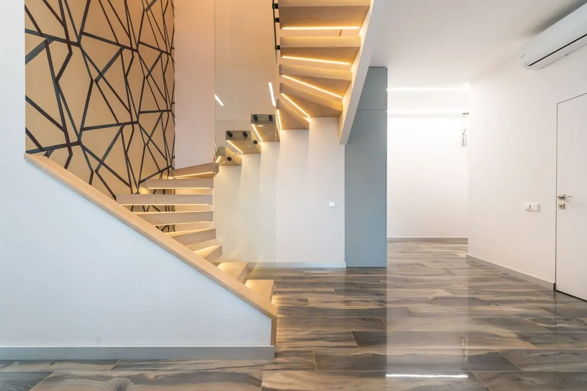 Neuer, leerer Innenraum mit beleuchteter Holztreppe und glänzendem Boden