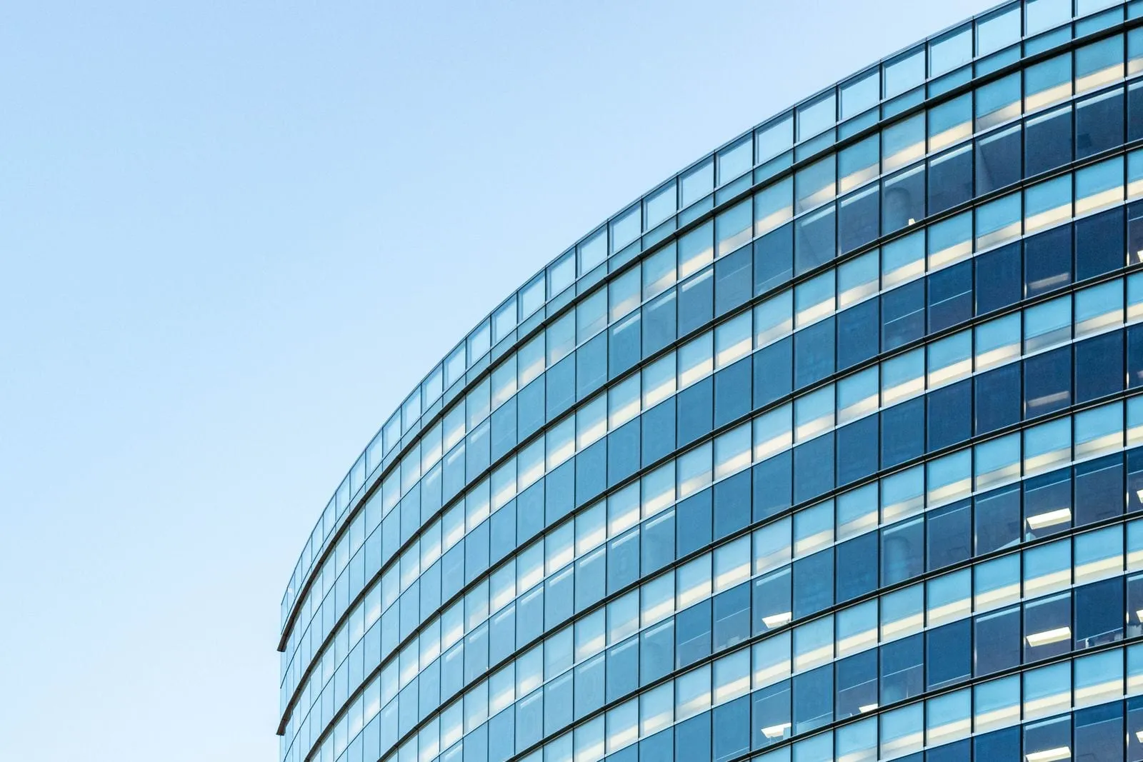 Modernes Bürogebäude mit geschwungener Glasfassade vor blauem Himmel